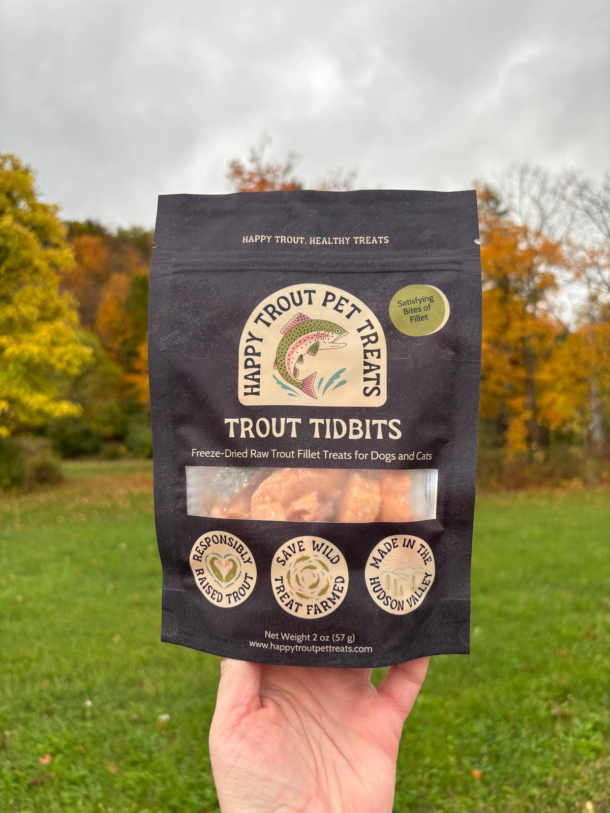 Hand holding a bag of Happy Trout Pet Treats Trout Tidbits in an autumn field