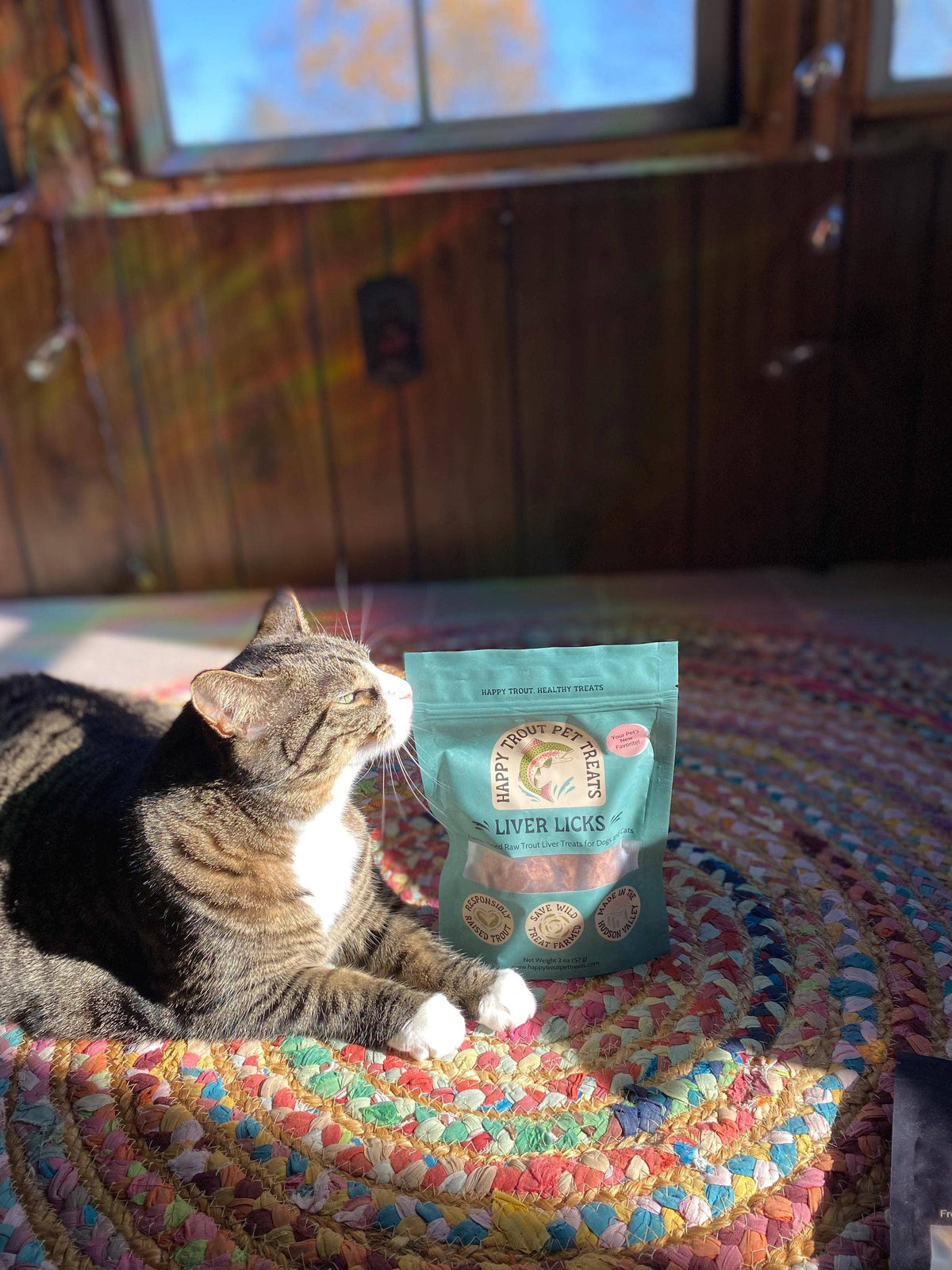 Tabby cat sitting beside a bag of Happy Trout Pet Treats Liver Licks