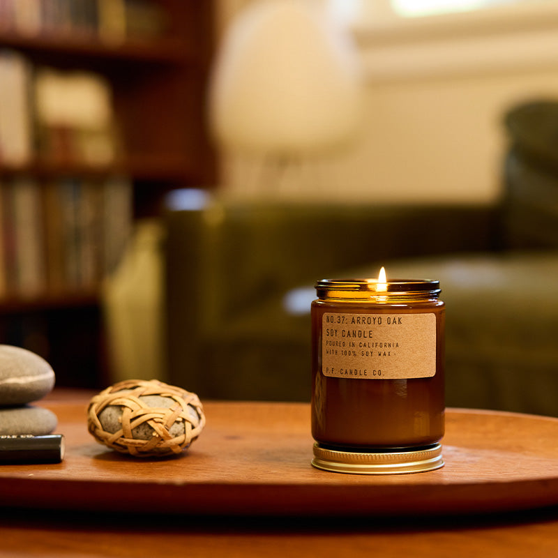 P.F. Candle Co. Standard Candle in Arroyo Oak lit on a wood tray in a living room