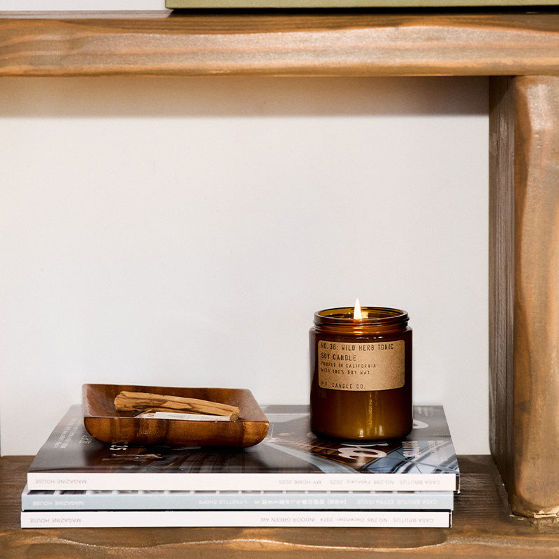 P.F. Candle Co. Standard Candle in Wild Herb Tonic on a wood shelf with a bowl and books