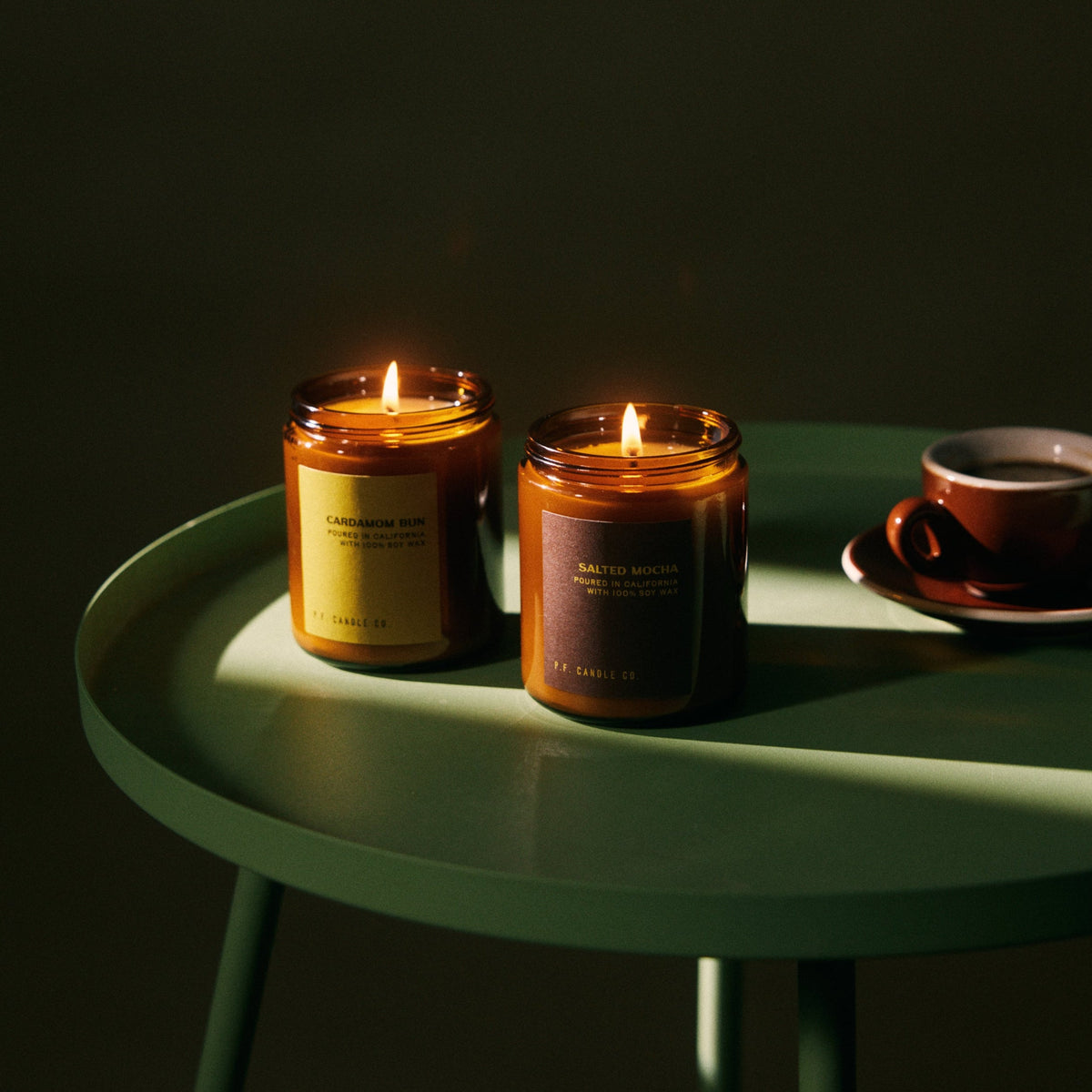 P.F. Candle Co. Cardamom Bun Standard Candle lit on a green side table