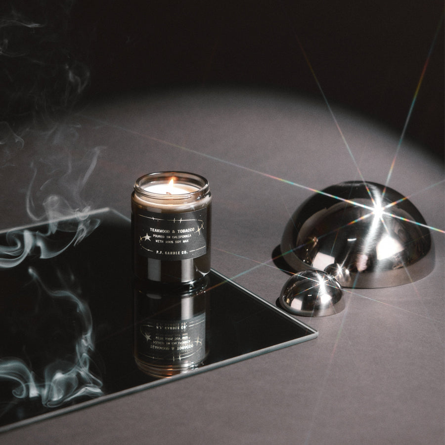 P.F. Candle Co. Celestial Collection Candle in Teakwood & Tobacco lit beside a chrome dome
